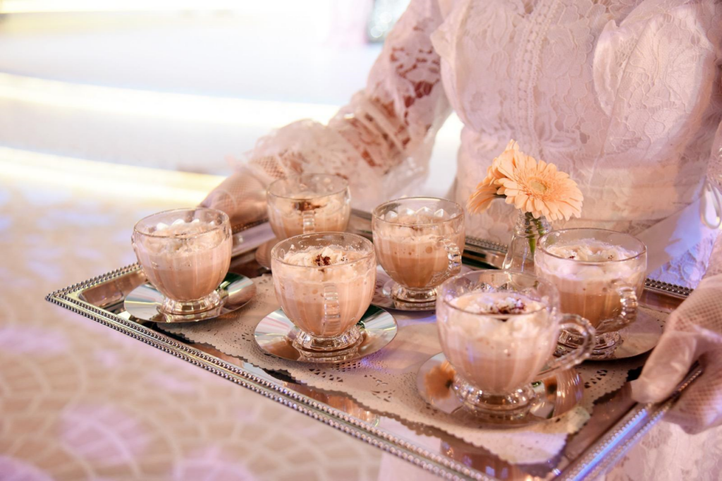 A woman in lace serves coffee drinks on a silver tray in a wedding setting, creating a luxurious atmosphere.